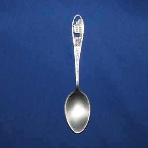 May include: Silver souvenir spoon with a detailed design of a building on the handle. The handle is engraved with the word "Hannibal".