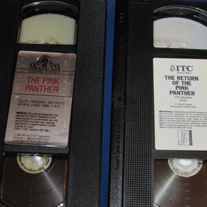 May include: Two black VHS tapes featuring the movies "The Pink Panther" and "The Return of the Pink Panther." The tapes have white labels with movie titles and logos. The tapes are in black plastic cases.