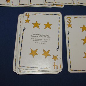 May include: A deck of Five Crowns playing cards. The cards are white with gold stars and blue and gold decorative borders. The number 4 and 3 are visible on the cards.