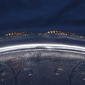 May include: A clear glass serving dish with a scalloped edge and a gold rim. The dish has a textured surface with a repeating pattern of small dots and swirls.
