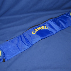 May include: A blue nylon carrying case with a zipper closure and a yellow "CAMEL" logo. The case has two yellow patches with a camel design.