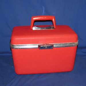 May include: A red vintage hard-sided carry-on suitcase with a silver metal trim and a red plastic handle.