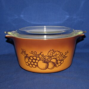 May include: A brown glass casserole dish with a clear glass lid. The dish has a brown and white design of grapes and apples.