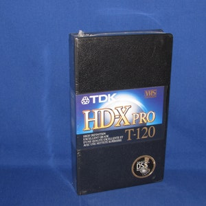 May include: Black VHS tape case with a silver TDK HDX Pro label. The label says "High Definition, Excellent Grade, T-120".