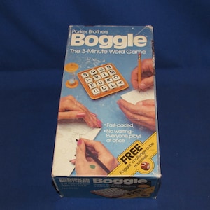 May include: A blue and yellow box for the board game Boggle, The 3-Minute Word Game by Parker Brothers. The box shows a close-up of the game board with letter cubes and a sand timer. The box also shows hands writing on paper and a pencil.