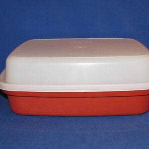 May include: A rectangular food storage container with a red base and a white lid. The lid has a slightly textured surface and fits snugly on the base. The container is made of durable plastic and is designed for food storage.