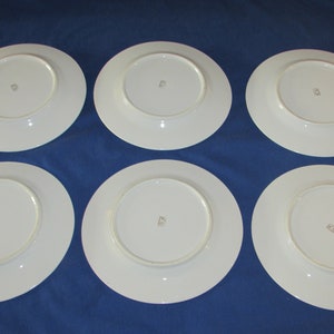 May include: Six white ceramic dinner plates with a gold rim and a small gold mark on the bottom.