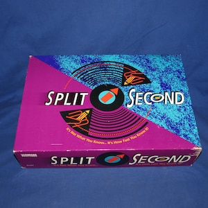 May include: A rectangular board game box titled Split Second with a diagonal split design. The left side is purple, and the right side features a blue textured pattern. The center displays a black circular graphic with the text It's Not What You Know... It's How Fast You Know It!