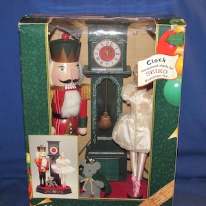 May include: A decorative clock with a nutcracker soldier and a ballerina figurine. The clock has a green frame and a round clock face. The nutcracker is wearing a red uniform and a tall hat. The ballerina is wearing a white dress and pink shoes. The text on the clock says "Clock movement made by SEIKO Precision Inc."