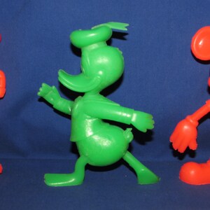 May include: Three vintage plastic cartoon character figurines. A red Goofy, a green Donald Duck, and a red Mickey Mouse.