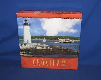 May include: A box for a 500-piece jigsaw puzzle by Croxley featuring a lighthouse and a boat on the water. The box has a red background with a white border and the text "Croxley" and "500 Fully Interlocking Pieces".