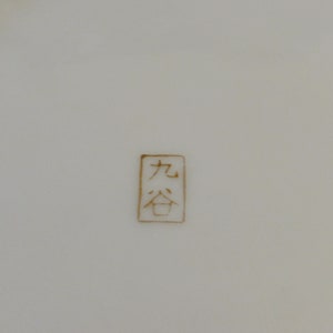 May include: A close-up of a white ceramic plate with a gold stamp that reads "九谷".