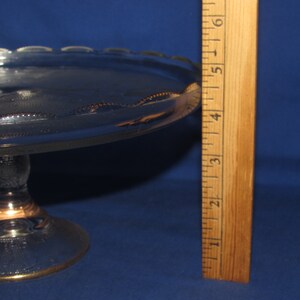 May include: A clear glass cake stand with a gold rim and a scalloped edge. The stand is 5 inches tall and has a diameter of 10 inches.