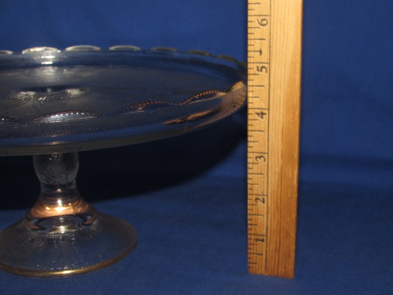 May include: A clear glass cake stand with a gold rim and a scalloped edge. The stand is 5 inches tall and has a diameter of 10 inches.