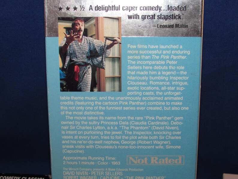 May include: VHS tape for the movie "The Pink Panther" featuring Peter Sellers. The cover has a photo of a man in a robe and text that reads "A delightful caper comedy...loaded with great slapstick."