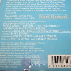 May include: A light blue VHS tape case for the movie "The Pink Panther" from 1963. The case features the film's title and cast, including David Niven and Peter Sellers. The case is marked "Not Rated".