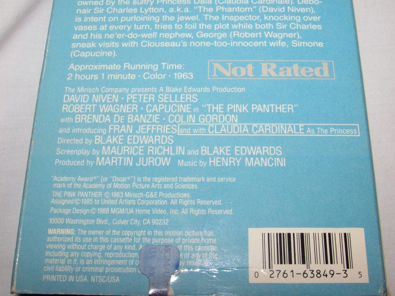 May include: A light blue VHS tape case for the movie "The Pink Panther" from 1963. The case features the film's title and cast, including David Niven and Peter Sellers. The case is marked "Not Rated".