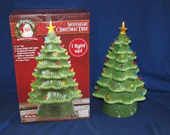 May include: A green ceramic Christmas tree with a gold star topper and multicolored faceted LED bulbs. The tree is displayed next to its original packaging box, which features the text Mr. Christmas Nostalgic Christmas Tree and I light up.