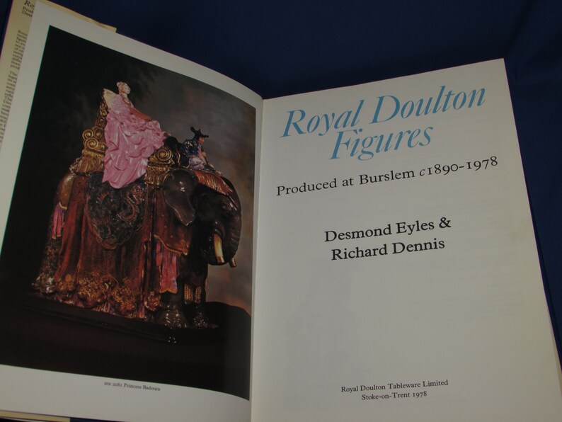 May include: A book titled "Royal Doulton Figures" with a photo of a porcelain figurine of a woman riding an elephant. The book cover text states "Produced at Burslem c1890-1978" and "Desmond Eyles & Richard Dennis".