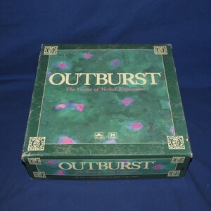 May include: A green board game box with the title "OUTBURST" in white lettering. The box has a mottled green and pink design. The game's subtitle, "The Game of Verbal Explosions," is also visible.