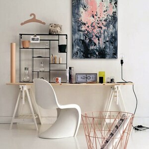 May include: A white desk with a white chair, a black metal shelf with the word "HELLO" on it, a pink and blue abstract painting, and a copper wire basket.