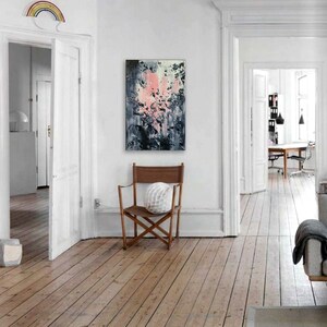 May include: Abstract painting with pink, white, and gray brushstrokes on a canvas. The painting is hanging on a white wall in a room with wooden floors.