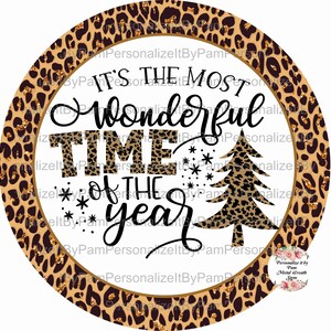 May include: A round, gold-rimmed, white background with a leopard print border. The text "It's the most wonderful time of the year" is written in black cursive font. A leopard print Christmas tree is in the centre of the design.