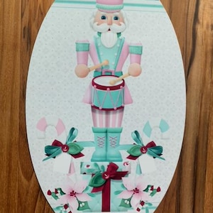 May include: A pink and green Christmas nutcracker playing a drum with candy canes and poinsettias on a black and white checkered background.