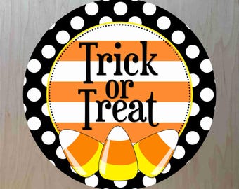 May include: A black and white polka dot circle with a yellow border. Inside the circle is an orange and white striped background with the text "Trick or Treat" in black. Three yellow and orange candy corn are at the bottom of the circle.