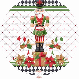 May include: A round Christmas ornament featuring a nutcracker soldier playing a drum. The nutcracker is standing on a stack of presents with poinsettia flowers and candy canes around the base. The background is a black and white checkered pattern with green and red stripes.