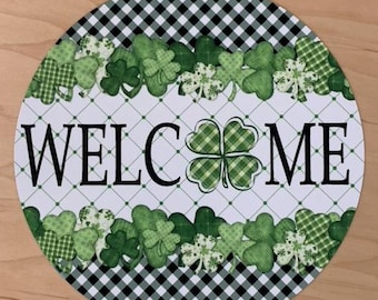 May include: Round welcome sign with a black and white checkered border. The center features a green shamrock with the word "WELCOME" in black lettering. The shamrock is surrounded by a border of green shamrocks.