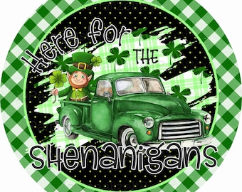 May include: A green truck with a leprechaun in the bed. The truck is on a black and white checkered background with green shamrocks. The text "Here for the Shenanigans" is written on the truck.