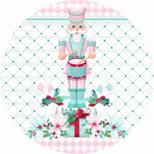 May include: A pink and blue Christmas ornament featuring a nutcracker playing a drum. The nutcracker is standing on top of a stack of wrapped presents with red bows and green holly.