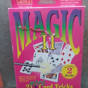 May include: A pink box of "MAGIC II" card tricks, featuring a deck of cards and a magic wand illustration. The box includes two decks of cards and an instruction booklet. The text reads "Learn Amazing Magic Tricks in Minutes!" and "more 21 Card Tricks."