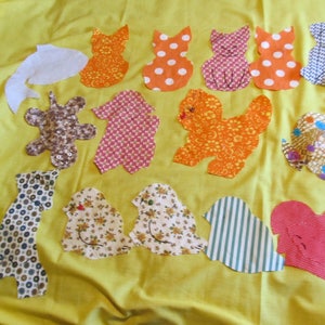 May include: A collection of colorful fabric cutouts in various animal shapes, including cats, dogs, and birds, arranged on a bright yellow background. The cutouts feature diverse patterns like polka dots, stripes, and floral prints, creating a playful and whimsical design.