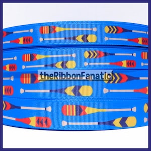 May include: Blue grosgrain ribbon featuring a repeating pattern of colorful oars in yellow, red, and navy blue. The ribbon has a textured surface and the text "theRibbonFanatic" is visible.