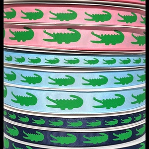 May include: A stack of green alligator patterned ribbon in various colors, including pink, blue, and navy blue. The ribbon is 1.5 inches wide and is perfect for crafting, decorating, and gift wrapping.