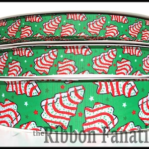 May include: A green grosgrain ribbon featuring a repeating pattern of white and red striped Christmas tree shapes, accented with small red and white stars. The ribbon has a textured, ribbed surface and is wound onto a spool for storage.
