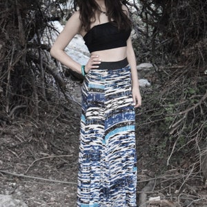 Könnte beinhalten: Eine Frau trägt ein schwarzes Crop-Top und einen langen, blau-weiß gemusterten Rock. Sie steht vor einem dunklen, grünen Hintergrund.