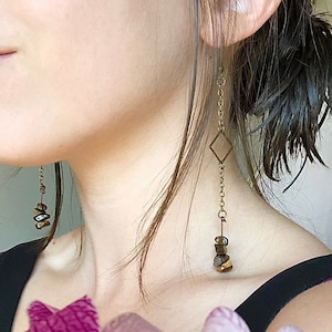 May include: Gold chain earrings with a square charm and brown tiger's eye stone beads.