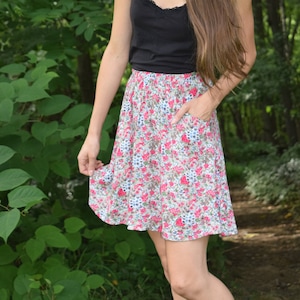 Peut inclure: Une femme portant un débardeur noir et une jupe à fleurs. Elle se tient dans une zone boisée avec une végétation verte.