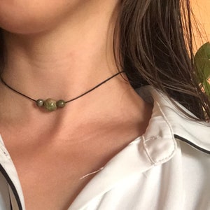 Peut inclure: Un collier ras de cou simple avec trois perles de pierres précieuses vertes.