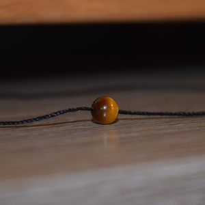 Peut inclure: Une seule perle en œil de tigre brun sur une ficelle noire.