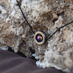 May include: A silver pendant necklace with a round, iridescent, black, and silver charm. The charm has a small, round, iridescent, purple, and blue center.