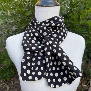 May include: A black silk scarf with a white button pattern. The scarf is tied around a white mannequin's neck.