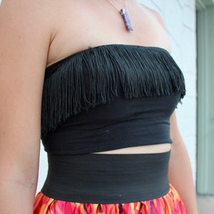 Peut inclure: Un haut noir sans bretelles avec une bordure en franges et une ceinture élastique noire. Le haut est porté avec une jupe colorée.