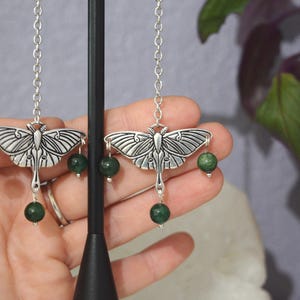 May include: Silver earrings with a moth design and green gemstone accents.