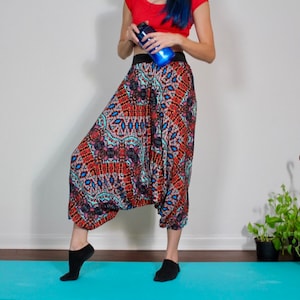May include: A person wearing colorful patterned pants with a black waistband and black socks. The person is standing on a blue yoga mat.