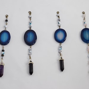 May include: Four agate stone pendants with different coloured crystal points hanging from gold chains. The agate stones are blue, white, and blue, and the crystal points are purple, black, black, and pink.