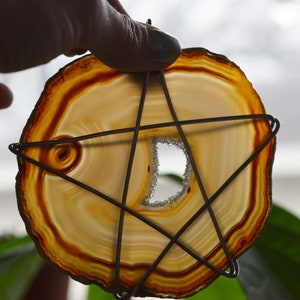 May include: A large, round, agate slice with a natural hole in the center. The agate is a mix of brown, orange, and white colors. A wire star is wrapped around the agate slice.